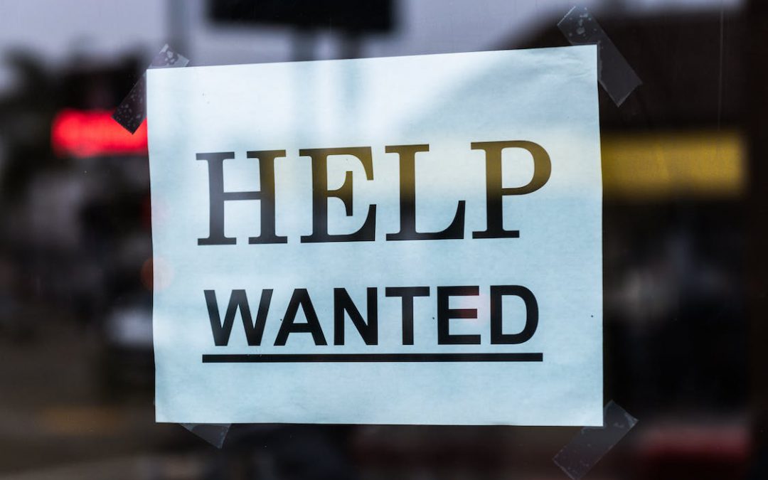 A sign taped to a window says Help Wanted